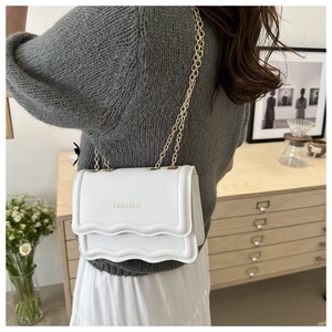 Gros plan d'un sac à bandoulière en cuir blanc avec coutures vagues et chaîne dorée