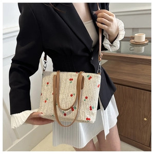 Detail of woven straw tote bag featuring red cherry embroidery and slim brown straps