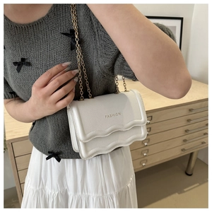Sac bandoulière blanc texturé avec chaîne dorée porté par un mannequin avec tenue