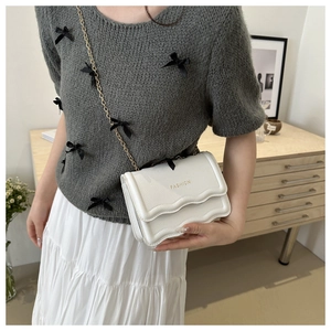 Détail d'un petit sac blanc à bandoulière chaîne dorée porté par un mannequin