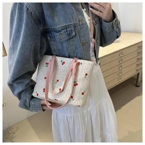 Detail of hand-woven straw tote bag with red cherry embroidery and pink handles