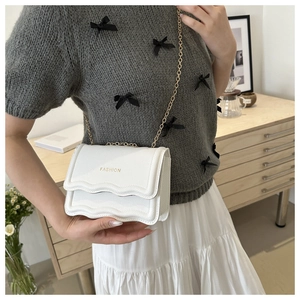 Détail du sac blanc à bords ondulés avec chaîne dorée et texture litchi sur un modèle