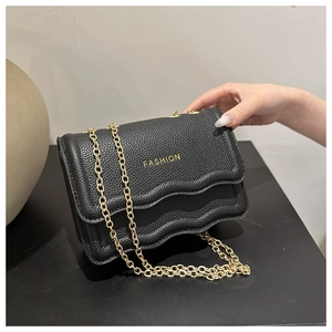 Détail du sac bandoulière en cuir noir avec rabat ondulé et bandoulière dorée