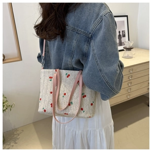 Detail of woven straw tote bag featuring cherry embroidery and pink leather straps