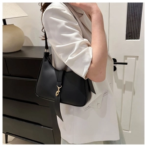 Detail view of a black crescent shoulder bag with golden metallic hook closure and matte finish