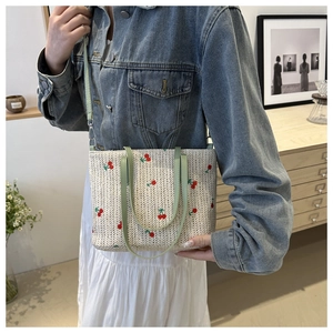 Detail of beige woven straw tote with red cherry embroidery and green leather handles