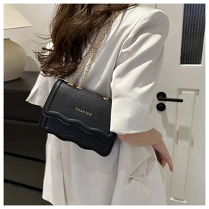 Détail du sac bandoulière en cuir noir avec rabat ondulé et bandoulière chaîne dorée
