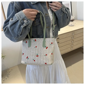 Detail of woven straw tote bag with red cherry embroidery and mint green handles