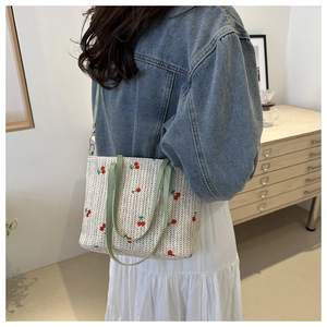 Detail of woven straw tote bag with red cherry embroidery and light green straps