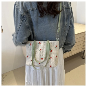 Detail of woven straw tote bag with cherry pattern and light green leather straps
