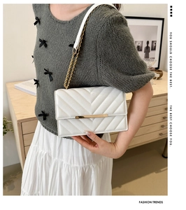 Close-up of white V-quilted shoulder bag with gold chain strap on grey knit sweater