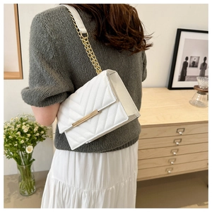 Detail of white crossbody bag with V-quilted texture and gold chain strap in a cozy interior