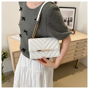 Detail of white quilted crossbody bag with golden metal trim and chain strap texture