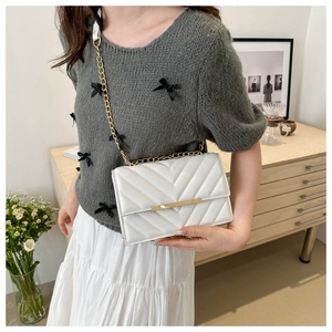 Close-up of white quilted shoulder bag with gold chain strap and v-shaped texture