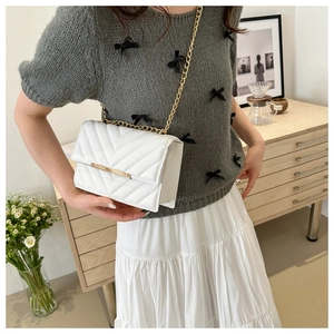 Close-up of white crossbody bag with lychee texture and gold V-shaped quilted details