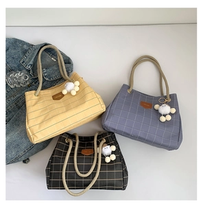 Close-up of checkered tote bags with rope handles, leather brand labels, and pom-pom charms