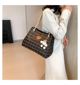 Close-up of brown checkered tote bag with woven rope handles and plush doll charm