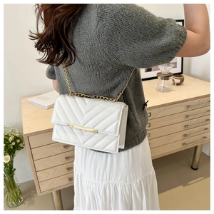 Detailed close-up of a white quilted shoulder bag with golden chain and V-pattern stitching