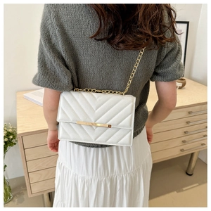 Detail of white chevron quilted faux leather bag with elegant gold chain strap and metal bar