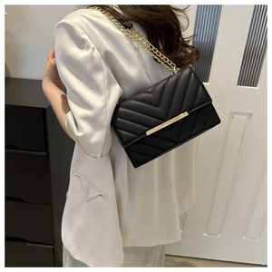 Close-up of black quilted shoulder bag with lychee texture and gold chain strap on a model