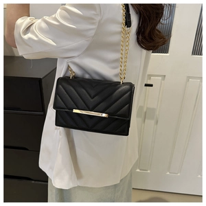 Detail of black V-quilted leather crossbody bag with gold chain strap on white blazer