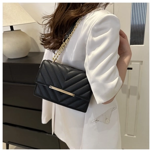 Rear view of black V-quilted leather crossbody bag with gold chain strap on a model