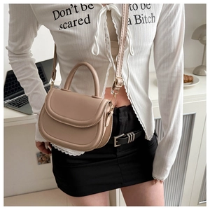 Detail of a beige leather saddle bag with round handle and adjustable shoulder strap