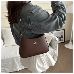 Deep brown matte leather underarm bag with silver star detail in a cozy home setting