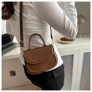 Detail view of a vintage brown saddle bag with gold hardware and curved handle