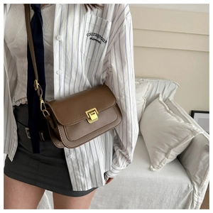 Close-up of brown textured leather crossbody bag with a gold metal clasp on a model