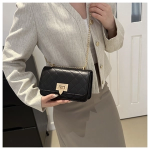 Close-up of black quilted shoulder bag with gold chain strap worn on the shoulder