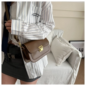 Brown leather crossbody bag with gold buckle shown on a model in a minimalist setting