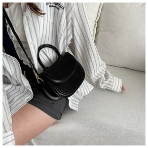Detail of a matte black PU leather saddle bag with gold metal buckles and top handle