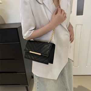Minimalist black quilted crossbody bag with gold chain strap shown on a female model