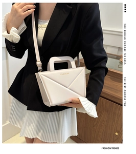 Detail of a minimalist cream crossbody bag with geometric design and golden branding