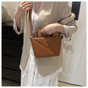 Brown handbag detail showing geometric folded lines and gold fashion lettering