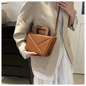 Nahaufnahme der karamellbraunen Handtasche mit geometrischer Faltung und Goldtext