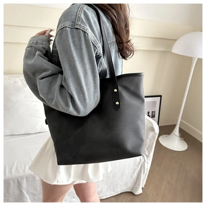 Close-up of black leather tote bag featuring elegant golden metal rivet details on straps