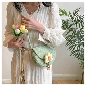 Green woven saddle bag with decorative fabric flower shown on a white dress