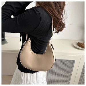 Detail view of a beige crescent bag worn on shoulder by model in a minimalist setting