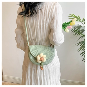 Detail of hand-woven mint green saddle bag featuring a 3D floral charm with tassel
