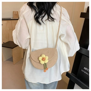 Detailed view of beige woven saddle bag with yellow flower charm worn by a model
