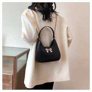 Détail du sac demi-lune en cuir noir avec nœud argenté et bandoulière en chaîne