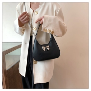 Close-up of a black leather underarm bag with a golden bow buckle and chain strap