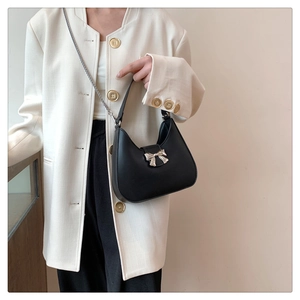Détail d'un sac bandoulière noir en croissant avec un nœud doré et une chaîne fine