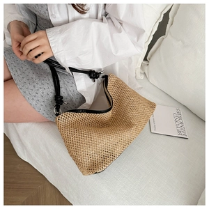 Detail of hand-woven straw bag with black leather shoulder strap and knot design