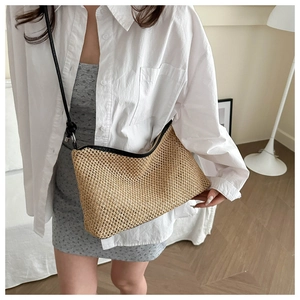 Detail of woven straw shoulder bag with black trim and adjustable strap on a model