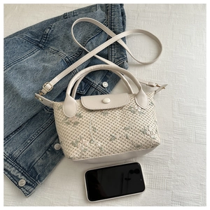 Detail of cream woven handbag with delicate floral embroidery and adjustable strap