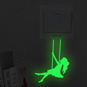 Luminous wall sticker showing a girl on a swing glowing green in a dark room