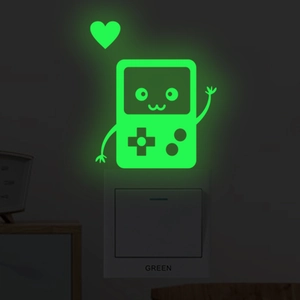 Luminous neon green cartoon game console sticker glowing on a wall switch in the dark
